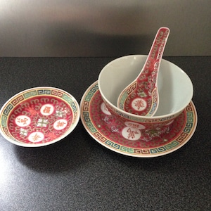 May include: A set of three red and white Chinese porcelain bowls with a decorative pattern. The set includes a large bowl, a small bowl, and a spoon. The bowls have a red and white floral design with Chinese characters.