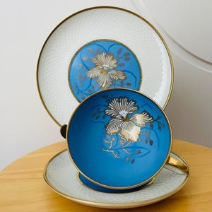 May include: A blue and white teacup and saucer set with gold floral accents. The teacup and saucer have a white background with a blue rim and a gold floral design. The saucer has a white background with a blue rim and a gold floral design.