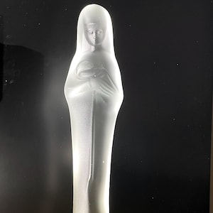 May include: A white glass figurine of the Virgin Mary holding a baby Jesus. The figurine is frosted and has a detailed design.