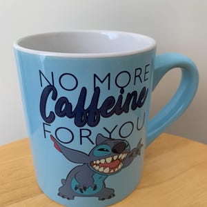 May include: A light blue ceramic mug with a cartoon Stitch character and the text "No More Caffeine For You".