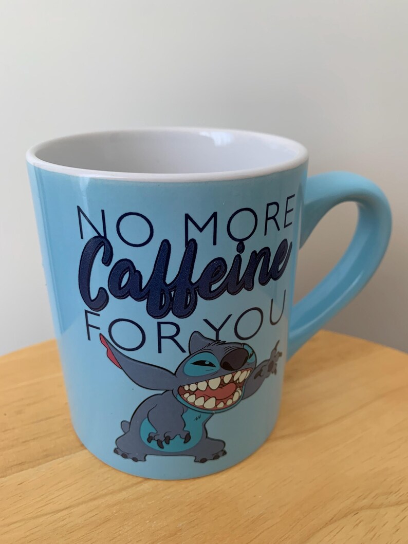 May include: A light blue ceramic mug with a cartoon Stitch character and the text "No More Caffeine For You".