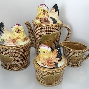 May include: A brown and white ceramic kitchen set featuring a chicken design. The set includes a coffee pot, sugar bowl, and creamer. Each piece has a woven basket design and a chicken lid. The coffee pot has the word "COFFEE" on it, the sugar bowl has the word "SUGAR" on it, and the creamer has the word "CREAM" on it.