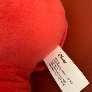 Puede incluir: Una etiqueta blanca con texto negro que dice "&copy;Disney Fabricado bajo licencia de Just Play, LLC 4850 T-Rex Ave, Suite 100 Boca Raton, FL 33431, USA".