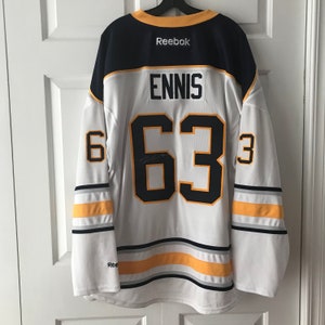 May include: White hockey jersey with blue and yellow accents. The number "63" is on the back with the name "ENNIS" above it. The Reebok logo is on the top front of the jersey.