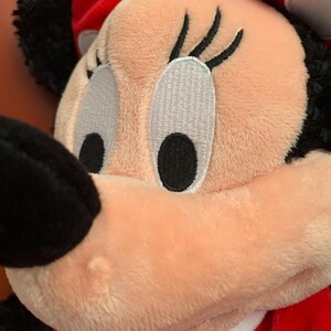 May include: A plush toy of a cartoon character with large black eyes, long eyelashes, and a pink nose. The toy is wearing a red dress with white polka dots and a white collar.