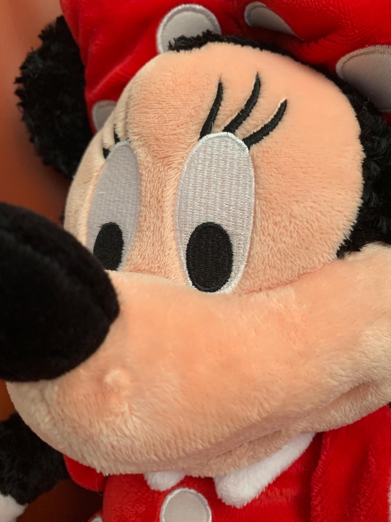 May include: A plush toy of a cartoon character with large black eyes, long eyelashes, and a pink nose. The toy is wearing a red dress with white polka dots and a white collar.