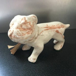May include: White ceramic bulldog figurine with brown marbling. The figurine is standing on all four legs and has a slightly tilted head. The figurine is signed "Max" on the bottom.