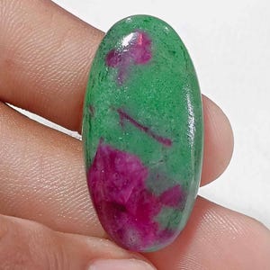 May include: An oval-shaped cabochon gemstone featuring a smooth, polished surface with a vibrant green base color and distinct, irregular patches of deep magenta and pink inclusions scattered throughout the stone's translucent crystalline structure.