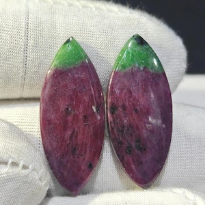 Puede incluir: Dos piedras preciosas de rubí zoisita en forma de marquesa, con un cuerpo de color magenta intenso y púrpura y una distintiva tapa verde vibrante. Las piedras tienen una superficie lisa y pulida con inclusiones oscuras naturales visibles.