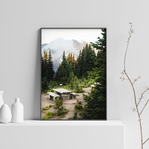 May include: A framed photograph of a mountain landscape with a wooden picnic table in the foreground. The mountain is covered in snow and the trees are green.