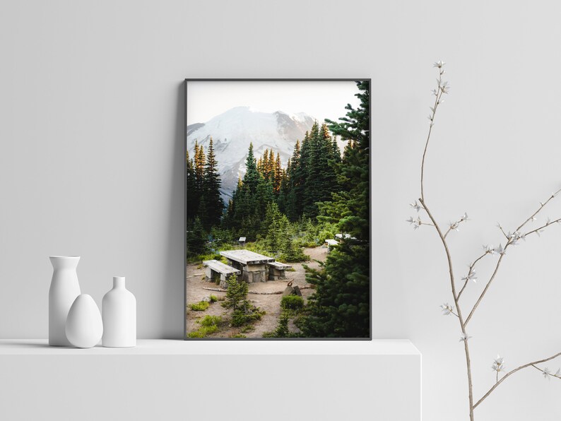 May include: A framed photograph of a mountain landscape with a wooden picnic table in the foreground. The mountain is covered in snow and the trees are green.