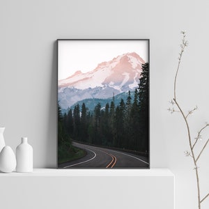 May include: A framed photograph of a winding road leading through a forest towards a snow-capped mountain peak. The mountain is a vibrant pink and blue color, with a clear sky above.