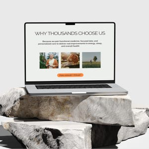 Puede incluir: Un port&aacute;til plateado que muestra el texto "WHY THOUSANDS CHOOSE US" y otro texto. El port&aacute;til est&aacute; sobre una pila de rocas de color gris claro. La pantalla muestra tres im&aacute;genes peque&ntilde;as y un bot&oacute;n que dice "Free consult (Virtual)".