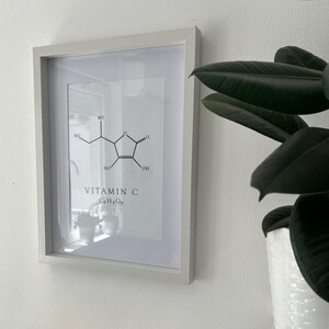 Pu&ograve; includere: Una stampa incorniciata con un'illustrazione in bianco e nero della struttura chimica della vitamina C, con il testo "VITAMIN C C6H8O6" sotto l'illustrazione.