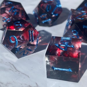 May include: Set of six red and black dice with blue numbers. The dice are made of clear resin with a swirling pattern. The numbers are raised and outlined in blue.