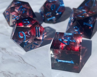 May include: Set of six red and black dice with blue numbers. The dice are made of clear resin with a swirling pattern. The numbers are raised and outlined in blue.