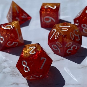May include: Set of eight red and gold dice with white numbers. The dice are made of a translucent material with a glittery finish.
