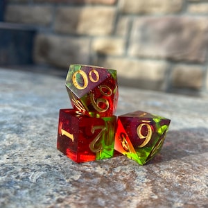 Può includere: Tre dadi rossi e verdi con numeri dorati. I dadi sono impilati uno sopra l'altro. Il dado superiore mostra il numero 0, il dado intermedio mostra il numero 1 e 7, e il dado inferiore mostra il numero 9.