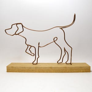 May include: A wire sculpture of a dog standing on an oak base. The sculpture is made of copper wire and is in the shape of a dog. The base is made of oak wood and is a natural colour.