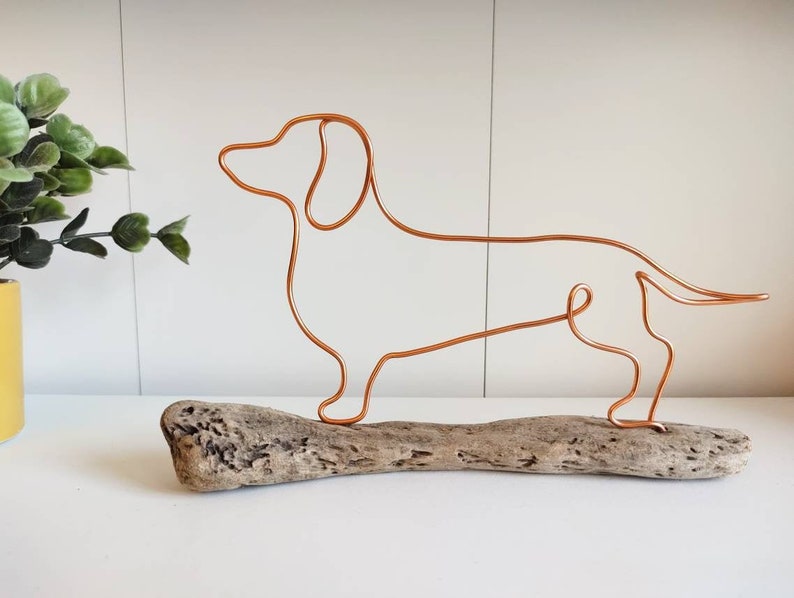 May include: A copper wire dachshund silhouette sculpture on a piece of driftwood.