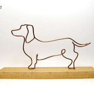 May include: A wire sculpture of a dachshund dog on a wooden base. The sculpture is made of copper wire and is a minimalist representation of a dachshund.