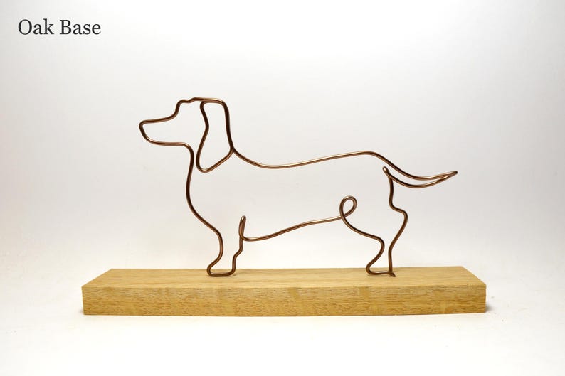 May include: A wire sculpture of a dachshund dog on a wooden base. The sculpture is made of copper wire and is a minimalist representation of a dachshund.