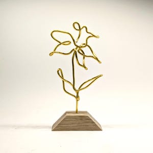 May include: A gold wire sculpture of a flower with a wooden base.
