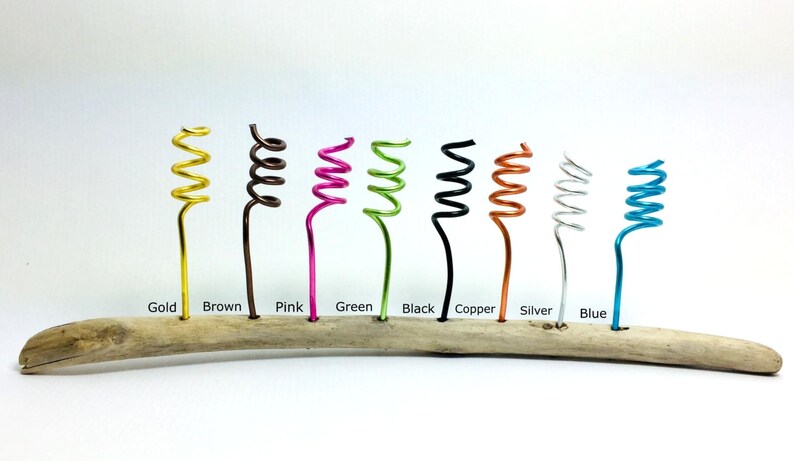 May include: A piece of driftwood with ten coiled wire stems in different colors: gold, brown, pink, green, black, copper, silver, blue, turquoise, and purple.
