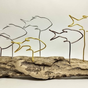 May include: A driftwood sculpture featuring six wire fish, each in a different colour: silver, gold, and copper. The fish are clustered together on the driftwood.