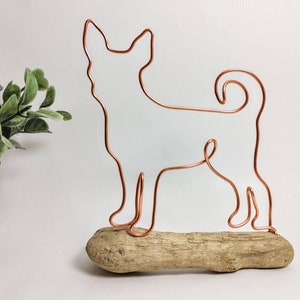 May include: A copper wire sculpture of a dog standing on a piece of driftwood.