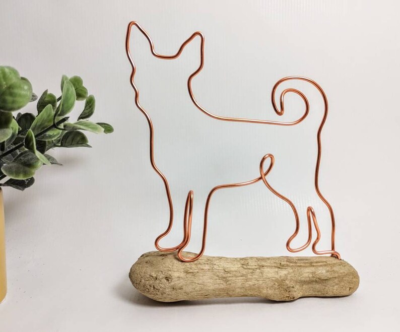 May include: A copper wire sculpture of a dog standing on a piece of driftwood.