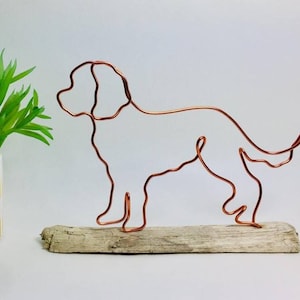 May include: A copper wire dog sculpture in a standing pose. The dog is made from a single continuous wire, mounted on driftwood. This decorative item is suitable for home decor or as a gift for dog lovers. The sculpture is a unique piece of art.