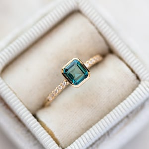 Könnte beinhalten: Ein goldener Ring mit einem türkisfarbenen Edelstein und einer Reihe kleiner Diamanten.