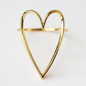 May include: A gold heart-shaped ring. The ring is made of a single piece of wire that is bent into a heart shape.
