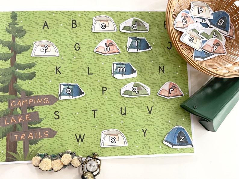 Puede incluir: Un gr&aacute;fico de alfabeto verde y marr&oacute;n con un tema de campamento. Las letras est&aacute;n impresas en im&aacute;genes con forma de tienda de campa&ntilde;a. El gr&aacute;fico incluye las palabras "Camping", "Lago" y "Senderos".