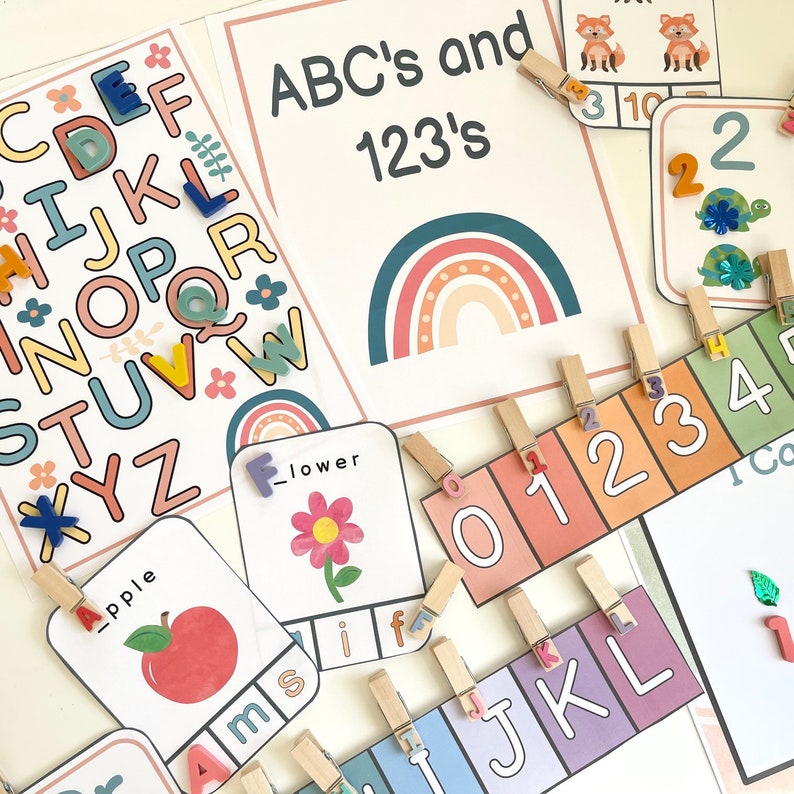May include: A set of colorful alphabet and number flashcards with rainbow and flower illustrations. The cards are designed for children to learn the alphabet and numbers. The cards are arranged on a white surface with wooden clothespins.