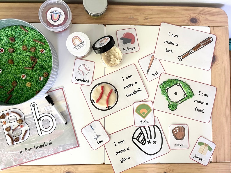 May include: A set of printable cards for a baseball-themed sensory bin activity. The cards feature images and text related to baseball, such as a bat, ball, glove, and field. The text on the cards reads "I can make a..." followed by the name of the item. The cards are printed on white cardstock with red borders.