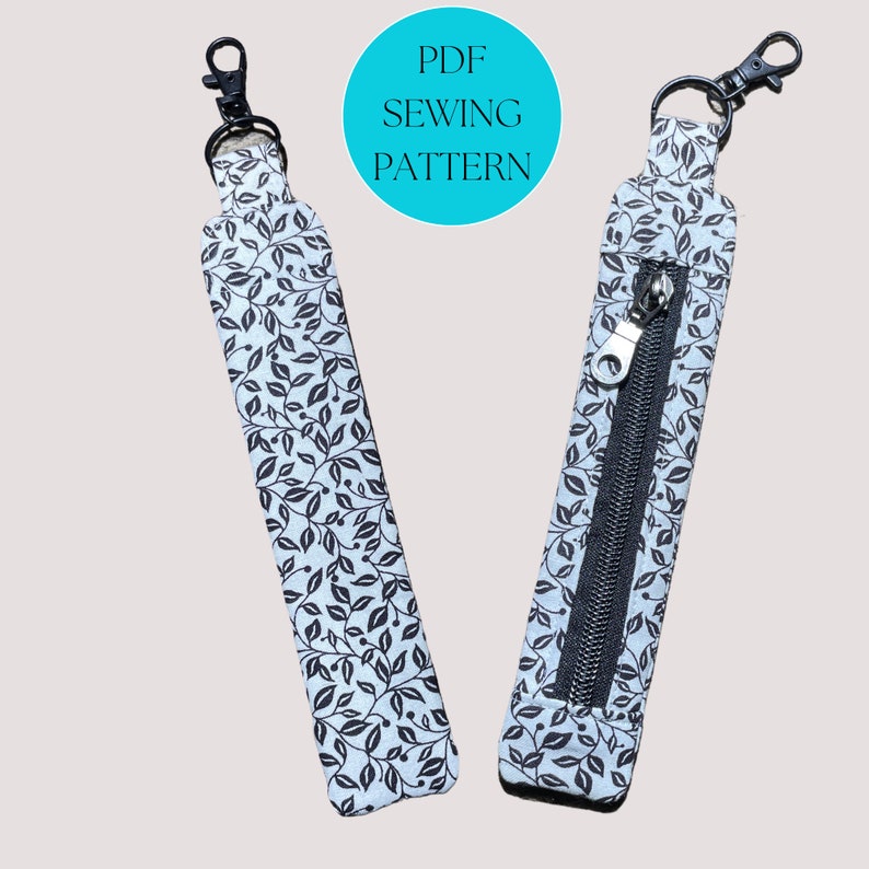 May include: A PDF sewing pattern for a key chain with a zippered pocket. The key chain is made of fabric with a black and white leaf pattern. The pattern is available for download.