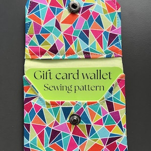 May include: A fabric wallet featuring a colorful geometric pattern of triangles in shades of pink, blue, orange, purple, and green. The wallet has a snap closure and contains a light green card with the text Gift card wallet Sewing pattern.