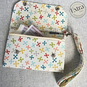 May include: Open white wallet with a colourful cross pattern. The wallet has a zipped pocket, snap closures, and a wrist strap. The interior reveals cash. The text "Extra Totes Sewing Patterns" is visible.