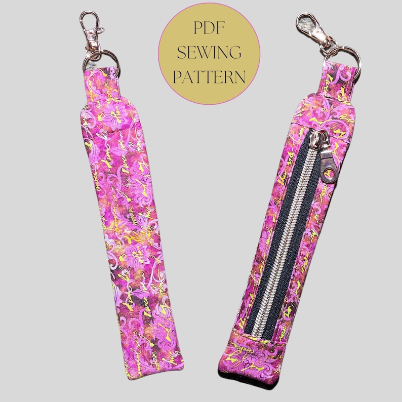 May include: A pink and gold floral patterned fabric key chain with a zippered pocket. The key chain has a silver metal clasp and a silver zipper. The image includes the text "PDF SEWING PATTERN".