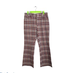 Könnte beinhalten: Eine braune und rote karierte Schlaghose, die an einem Kleiderbügel hängt. Die Hose hat eine weite Beinöffnung und ein klassisches Karomuster.