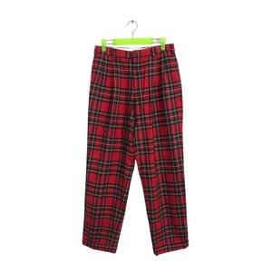 May include: Red plaid pants with a black and yellow plaid pattern. The pants are hanging on a green hanger.