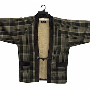 May include: A plaid kimono-style jacket in shades of green, brown, and tan, with a plush, cream-coloured interior lining. The jacket features black trim, pockets, and a toggle closure. The garment is displayed on a black hanger.