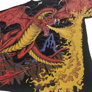 May include: Black t-shirt featuring a detailed illustration of a red dragon breathing fire. The dragon has large wings and sharp teeth, with a castle in the background. The flames are yellow and orange.