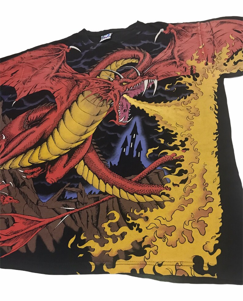 May include: Black t-shirt featuring a detailed illustration of a red dragon breathing fire. The dragon has large wings and sharp teeth, with a castle in the background. The flames are yellow and orange.
