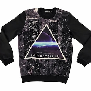 May include: Black sweatshirt featuring a cityscape design with a triangular graphic of a planet and the text "INTERSTELLAR". The long-sleeved top has black sleeves and a crew neck.