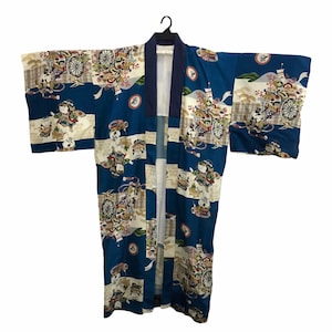 May include: A blue Japanese kimono with a decorative pattern featuring figures, carts, and floral elements. The kimono has a dark blue collar and trim, and is hanging on a black hanger. The design is repeated across the fabric.