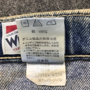 May include: Close-up of a denim jeans label with Japanese text. The label shows washing instructions, fabric composition, and product details. The brand name "Wrangler Japan" is visible.