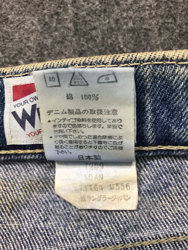 May include: Close-up of a denim jeans label with Japanese text. The label shows washing instructions, fabric composition, and product details. The brand name "Wrangler Japan" is visible.